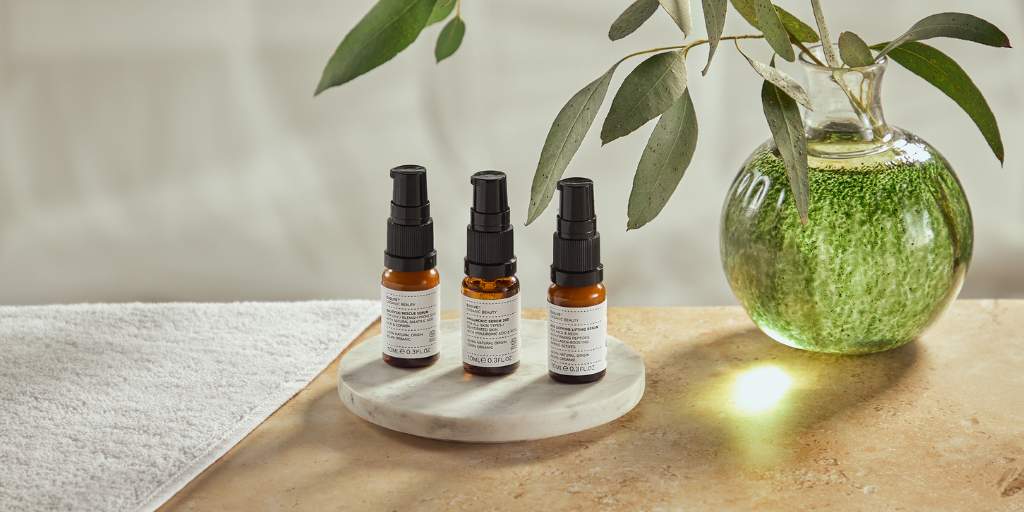 three serums on marble tray next to plant in green glass jar with light shining through