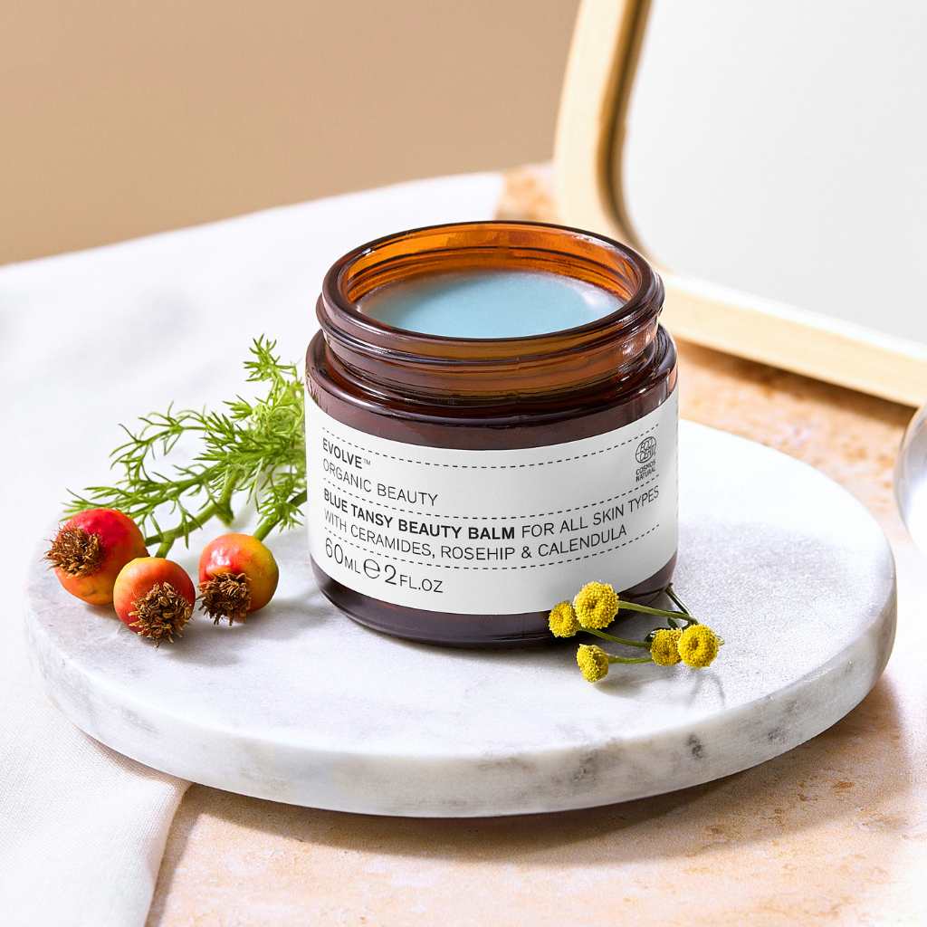 blue tansy beauty balm evolve organic skincare on marble coaster with yellow flowers and rosehips